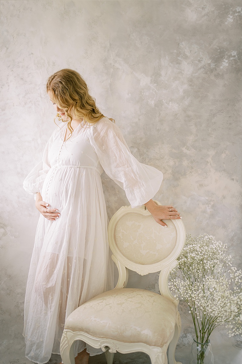 studio maternity photography session in Brisbane, AUS with custom hand-painted backdrop by Hikari Lifestyle Photography featured on The Motherhood Anthology pregnant mama in studio with florals